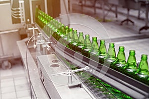 Automated conveyor line in a brewery. Rows of green glass bottles on a conveyor belt.
