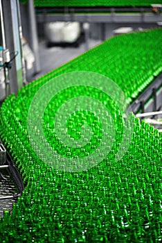 Automated conveyor line in a brewery. Rows of green glass bottles on a conveyor belt.