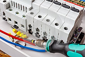 Automatic circuit breakers installed on DIN rail in white plastic mounting box on a background of wires and screwdriver