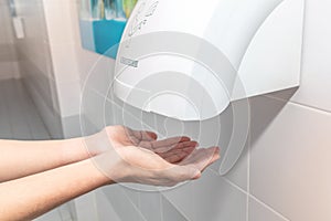 Automatic hand dryer in public toilet or restroom hygiene concept. A man hands using utomatic hand dryer in bathroom