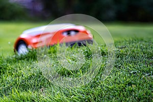 Automatic lawn robot mower drives up to the grass slope, lawn. Intentionally blurred mower. Close up side view, with sharp grass