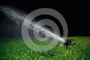 Automatic lawn sprinkler spraying water over golf course green grass