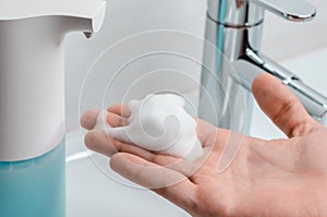 Automatic soap dispenser in the bathroom. Hand with soapy solution closeup