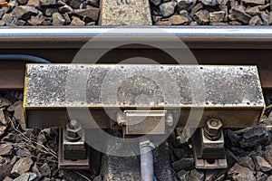 Automatic train braking system mounted on railway tracks, visible concrete sleepers and large stones between them.
