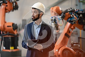 Automation engineer uses tablet for programming robotic arm in factory.