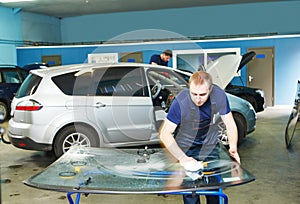 Automobile glazier cleaning car windscreen or windshield in service garage