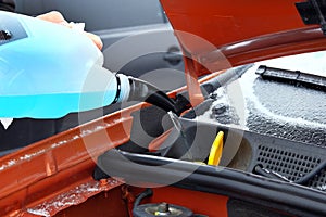 Automobile maintenance concept. Filling blue windshield washer fluid on car in winter. Close up