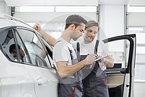 Automobile mechanics checking checklist while standing by car in workshop