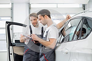 Automobile mechanics checking checklist while standing by car in workshop