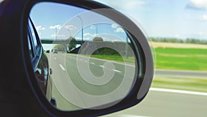 Automobile in motion. View in the rear view side mirror of a auto, driving a red car along the track