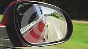 Automobile in motion. View in the rear view side mirror of a auto, driving a red car along the track