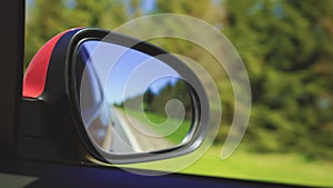 Automobile in motion. View in the rear view side mirror of a auto, driving a red car along the track