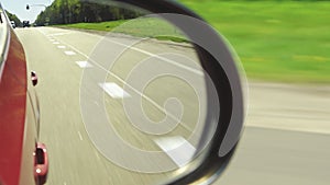 Automobile in motion. View in the rear view side mirror of a auto, driving a red car along the track