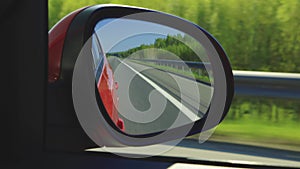 Automobile in motion. View in the rear view side mirror of a auto, driving a red car along the track
