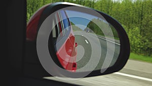 Automobile in motion. View in the rear view side mirror of a auto, driving a red car along the track