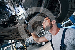 Automobile repairman examining car underside using flashlight