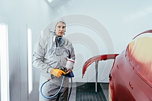 Automobile repairman painter hand in protective glove with airbrush pulverizer painting car body in paint chamber.