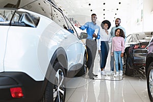 Automobile seller showing luxury car to young black family at auto dealership