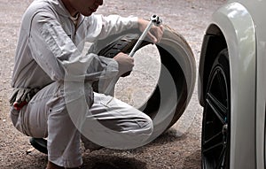 Automotive mechanic man in uniform with tire and wrench for fixing car at the repair garage background.