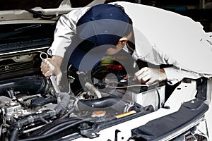 Automotive mechanic in uniform with wrench diagnosing engine under hood of car at the repair garage.