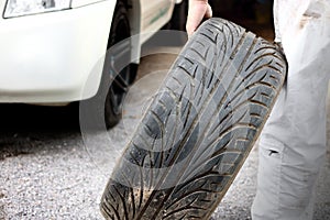 Automotive mechanic in white uniform holding tire for fixing at the repair garage background. Car insurance concept.