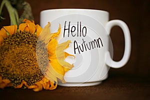 Autum coffee concept with yellow sunflower closeup. White mug of coffee with text - Hello Autumn