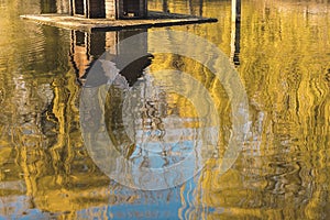 Autumn abstract pond water surface with reflection from September yellow trees foliage and wooden cabin house for birds park