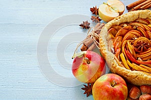 Autumn apple pie on the wooden board decorated with fresh apples, hazelnuts, spices - anise, cinnamon on the gray kitchen table