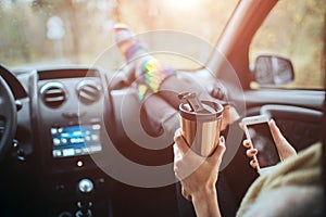 Autumn, Auto travel. Cose-up of a woman drinking take away cup coffee during the road trip in a car. Woman feet in warm