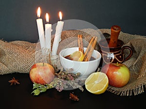 Autumn background with apples, pear, dried herbs, anise, cinnamon sticks, a cup of tea, candles, sackcloth.