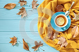 Autumn background concept - blue cup of black tea with lemon slice and honey on a yellow scarf, dried leaves on a blue wooden back