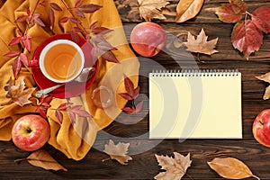Autumn background concept - red cup of tea with piece of lemon, dried leaves, red apples, honey and empty notebook for text on a w