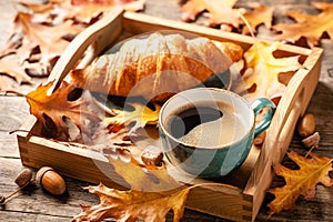Autumn background with cup of black coffee, croissant and fall oak leaves