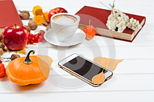 Autumn background, cup of cappuccino, mobile phone on wooden table.