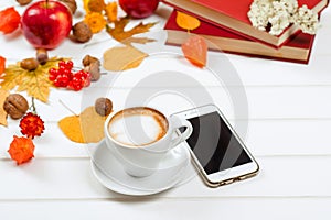 Autumn background, cup of cappuccino near mobile phone on wooden table.