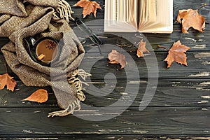 Autumn background. Cup of coffee, lambswool scarf, eyeglasses, open book, maple leaves on black wooden background, top