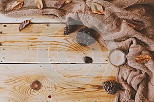Autumn background. A cup of hot coffee, knitted scarf and pinecones on wooden table. Autumn coffee drink. Top view. Copy space