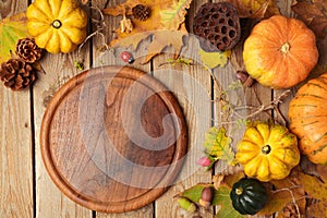 Autumn background with cutting board, fall leaves and pumpkin over wooden table.