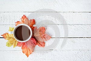 Autumn background with dry leaves and hot cup of coffee on white wooden table, copy space. Top view