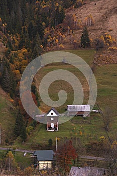 Autumn background in the mountains. Hills covered with yellow trees and houses