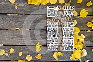 Autumn background. Wooden carved word of the Lord`s Prayer on a shabby wooden board with yellow leaves
