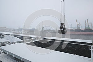 Autumn bad weather, snow, loading coal into the holds of industrial ships in the seaport