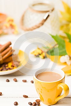 Autumn banner with cup of coffee with cinnamon on white wooden background with colorful tree leaves.