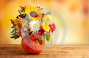 Autumn bouquet of beautiful flowers and berries in a pumpkin on wooden  table. Concept of autumn festive decoration for