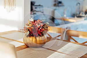 Autumn bouquet of bright artificial flowers in a golden pumpkin vase on a kitchen table counter with white modern