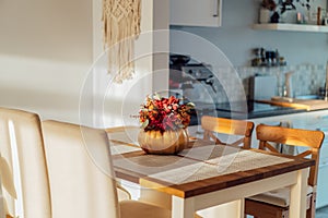 Autumn bouquet of bright artificial flowers in a golden pumpkin vase on a kitchen table counter with white modern