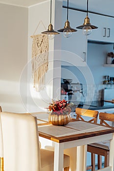 Autumn bouquet of bright artificial flowers in a golden pumpkin vase on kitchen table counter with white modern kitchen