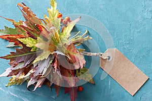 Autumn bouquet of leaves with blank tag on turquoise background