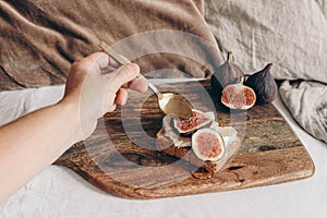 Autumn breakfast in bed composition.Closeup of hand puring honey over bread with brie cheese and fig fruit. Wooden chop