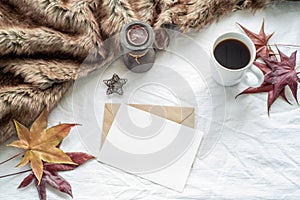 Autumn breakfast scene. Blank greeting card, invitation card mockup with maple leaves, cup of coffee, scented candle and plaid.